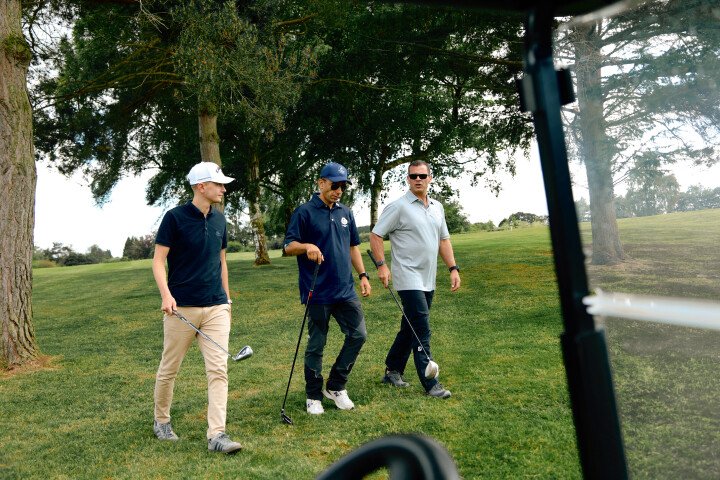 Picture of 3 people walking on grass with golf clubs